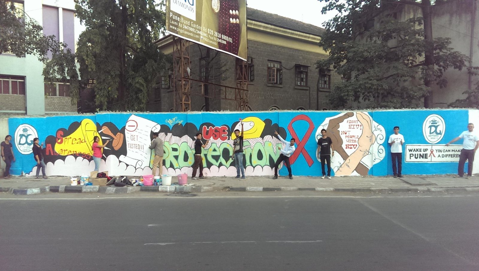 Corporate employee engagement CSR activity where volunteers painted a roadside wall with awareness designs on HIV and AIDS prevention, promoting social responsibility, health education, and community impact.